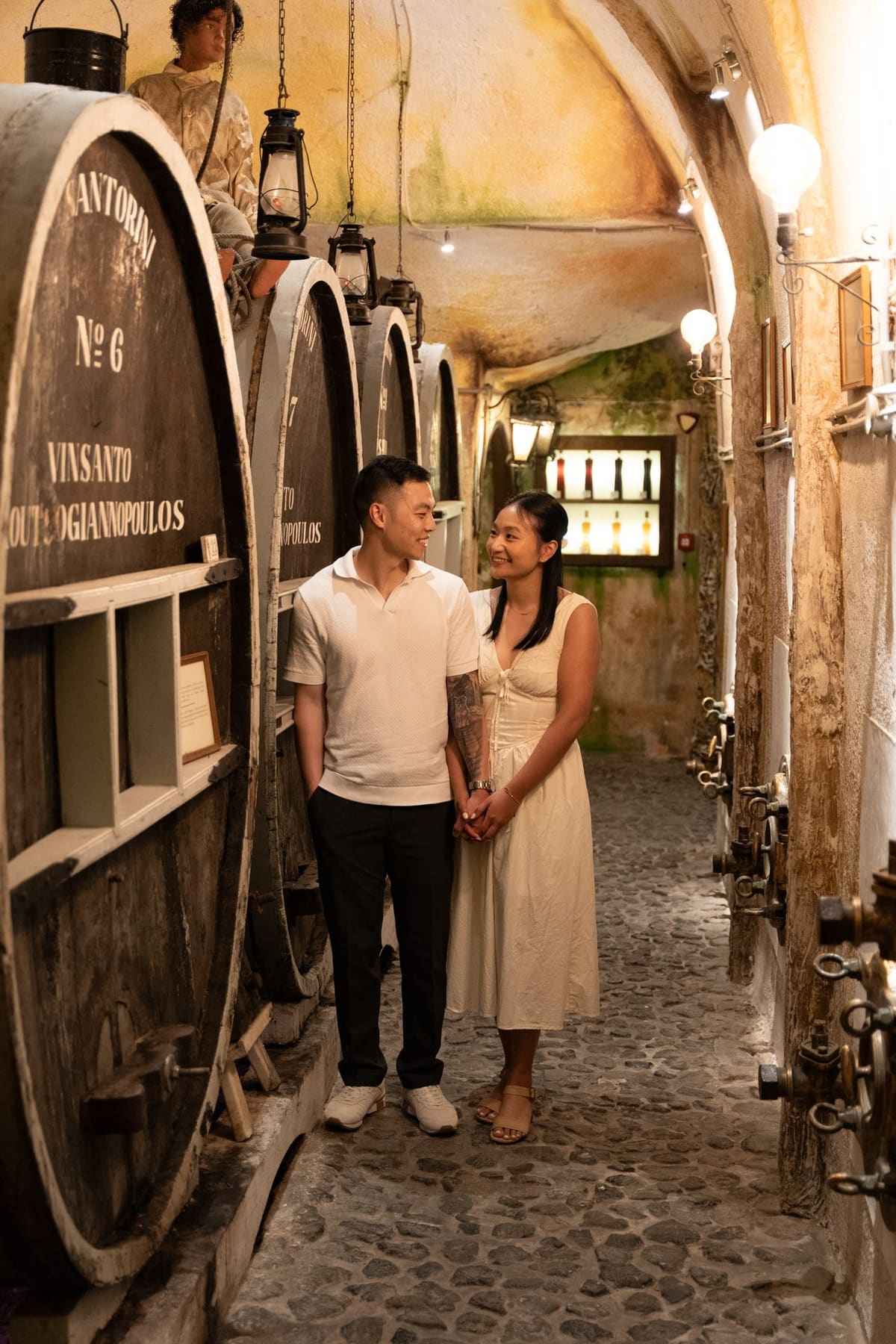 Couple in white among oak barrels in a traditional Santorini wine cellar