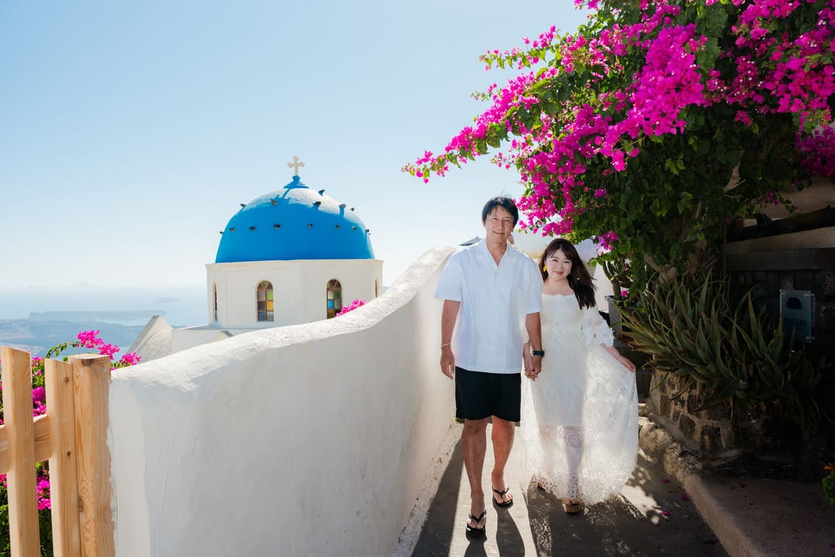 Family of three in front of the blue dome of Oia framed by pink bougainvillea