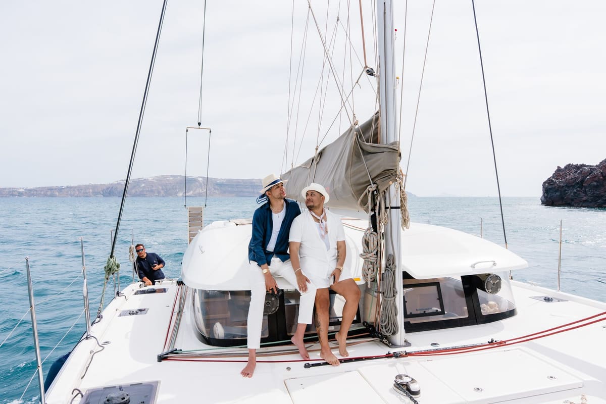 Couple seated on the bow of a sailing catamaran crossing the Santorini caldera