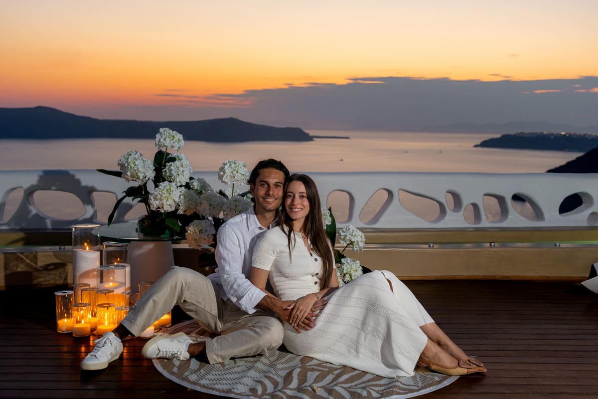 Couple relaxing with drinks on a Fira terrace as the sunset turns orange, Santorini