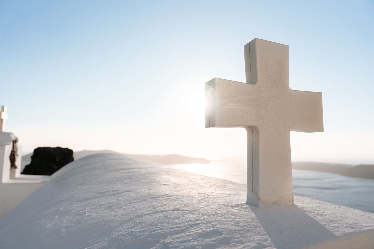 The white cross of the Agios Georgios chapel below Skaros Rock, backlit by the low sun