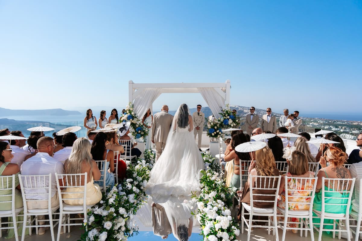 Bride walking down a mirrored aisle toward the caldera at a Santorini clifftop wedding