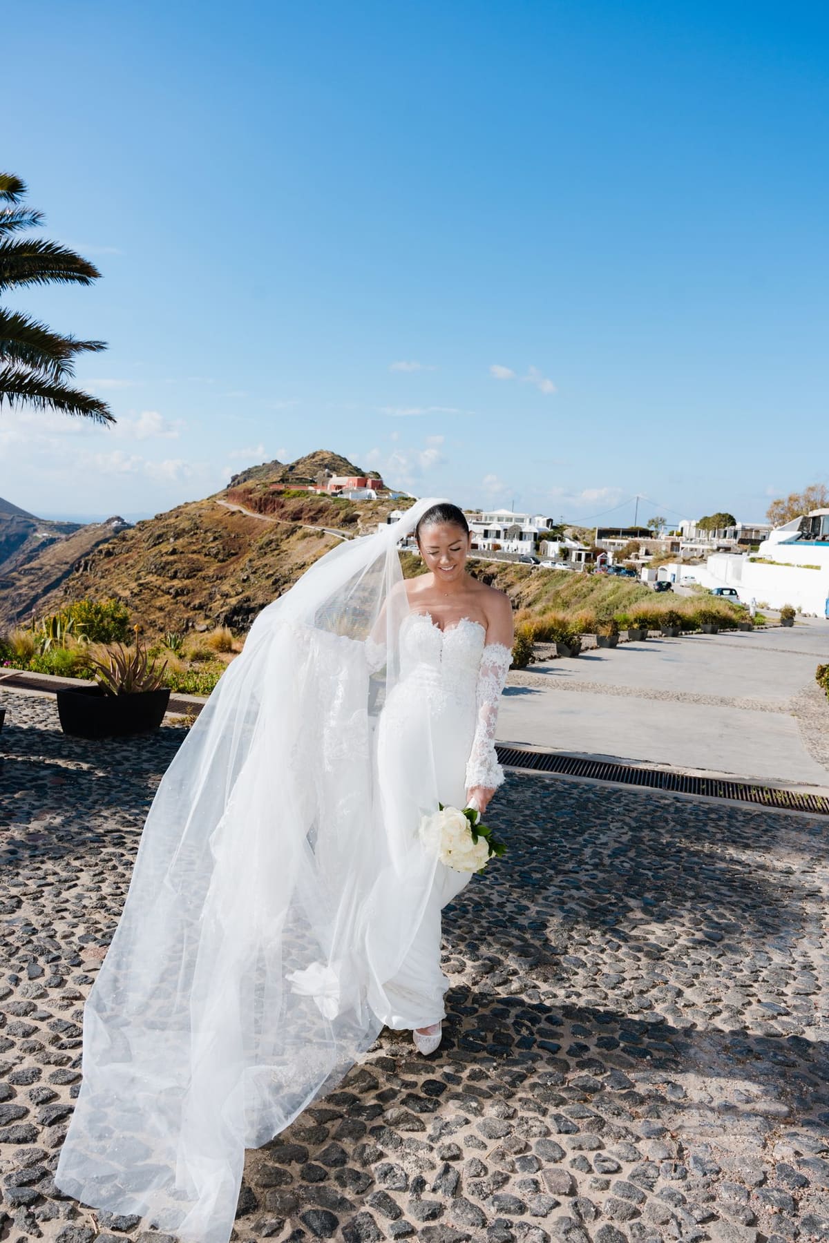 Bride with a long veil walking along a cobbled path in Oia, Santorini