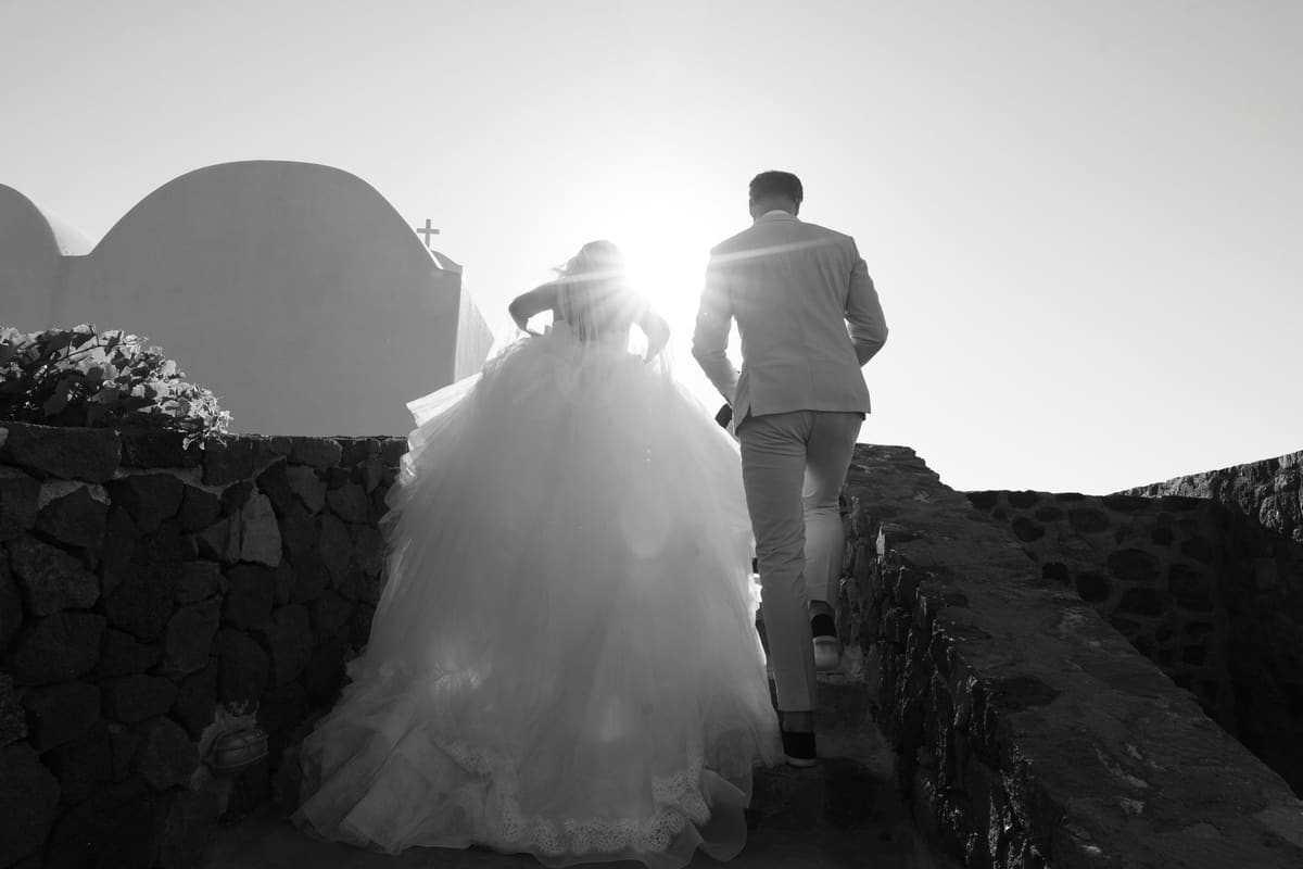 Newlyweds walking up the chapel steps into the sun, black and white, Santorini